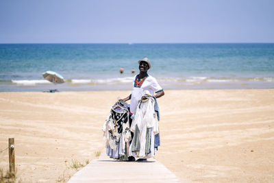 Male vendor standing on boardwalk while selling clothes at beach during sunny day