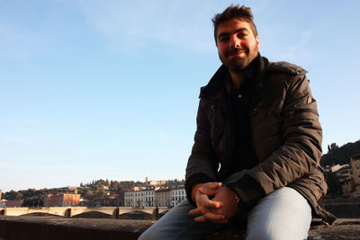 Portrait of man sitting against sky in city