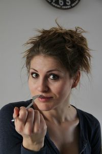 Close-up portrait of woman with fork in mouth sitting against wall at home