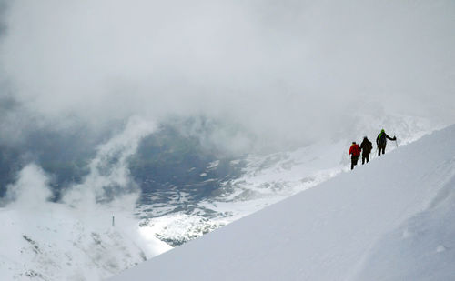 Hikers on snow covered mountain against sky