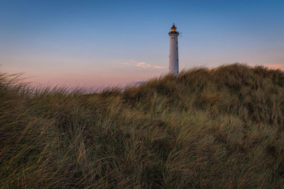 Lighthouse on field against sky at sunset