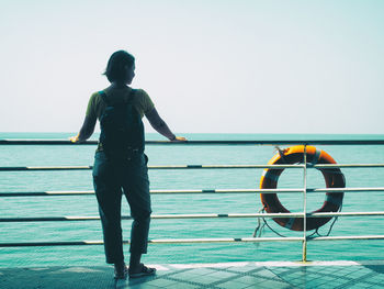 Rear view of woman standing by railing of boat in sea against clear sky