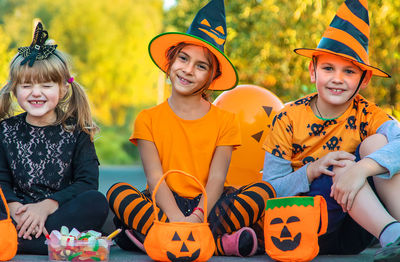 Portrait of smiling girls wearing halloween hats sitting on road