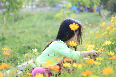 Rear view of girl with yellow flowers on field