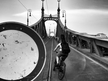 Rear view of people riding bicycle on bridge