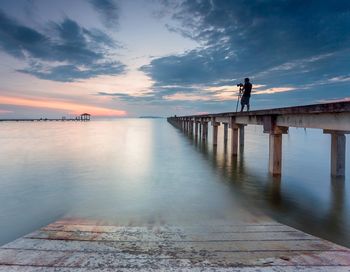 Man standing on pier over sea against sky during sunset