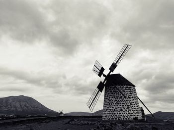 Traditional windmill on landscape against cloudy sky