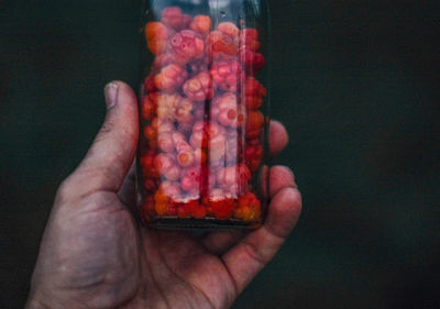 Cropped hand holding caviar in bottle against black background