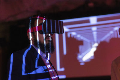 Bearded businessman wearing futuristic glasses in illuminated exhibition center