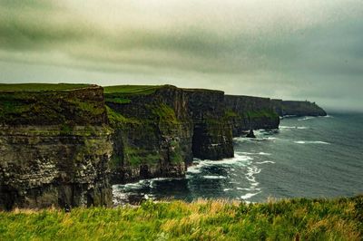 Scenic view of rocky coastline against cloudy sky