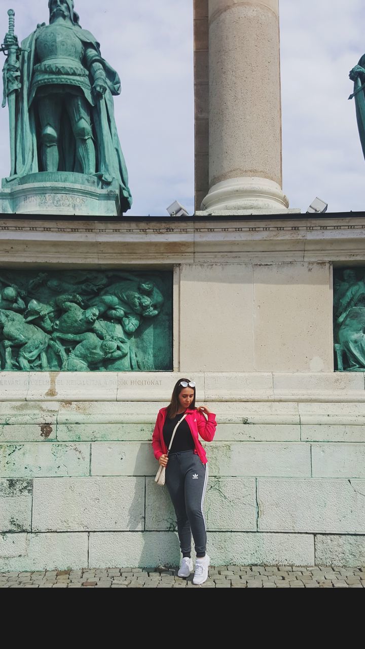 architecture, building exterior, built structure, real people, one person, lifestyles, front view, young adult, portrait, young women, full length, day, leisure activity, casual clothing, looking at camera, standing, women, adult, clothing, architectural column, outdoors, warm clothing