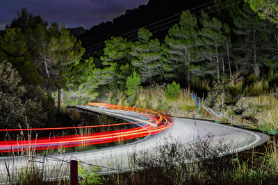 Light trails on road by trees against mountain