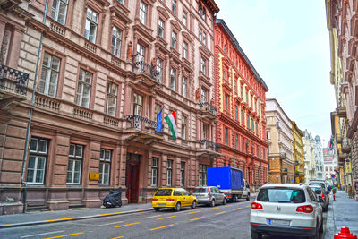 Cars on city street by buildings against sky