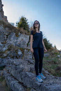 Portrait of young woman standing on rock against clear sky