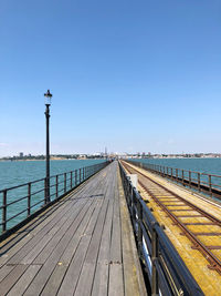 Pier over sea against clear blue sky