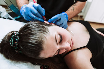 Crop unrecognizable male tattooist making marks on ear of female customer before applying tattoo during work in modern salon