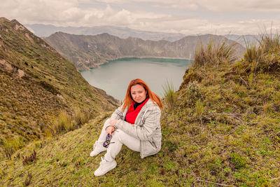 Portrait of smiling young woman sitting against mountains