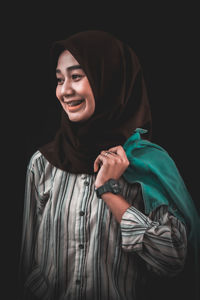 Portrait of smiling young woman against black background