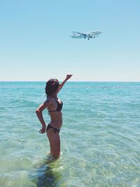 Full length of young woman flying over sea against clear sky