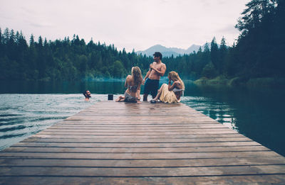 People sitting on pier over lake against sky