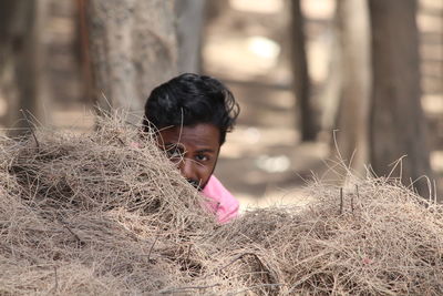 Portrait of man hiding by grass in forest