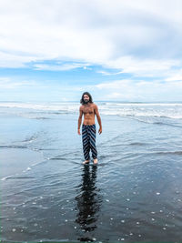 Full length of shirtless man standing in sea against sky