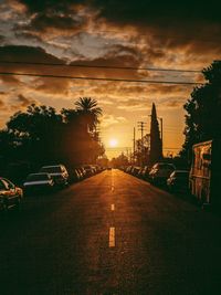 Cars on road by buildings against sky during sunset