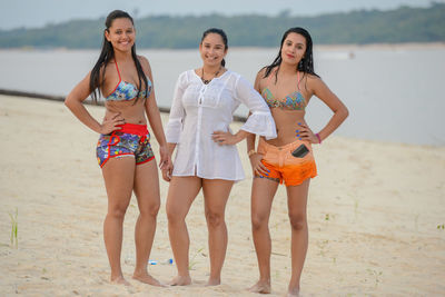 Portrait of happy female friends with hands on hip standing at beach