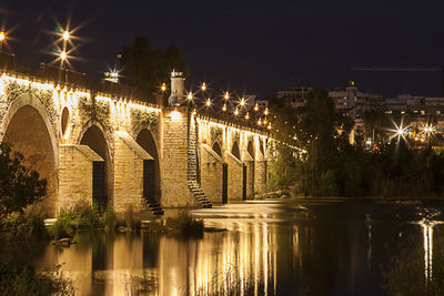 Illuminated bridge over river against sky at night