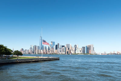 Sea by modern buildings against clear blue sky