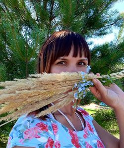 Portrait of woman holding plant against trees