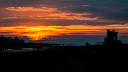 Silhouette of cityscape against dramatic sky during sunset