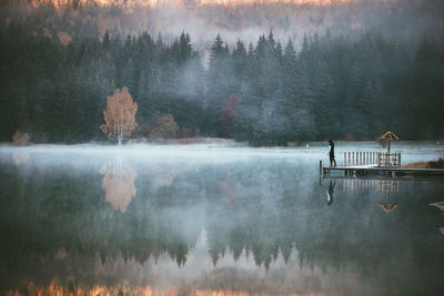 Distant view of man on jetty over lake with reflection