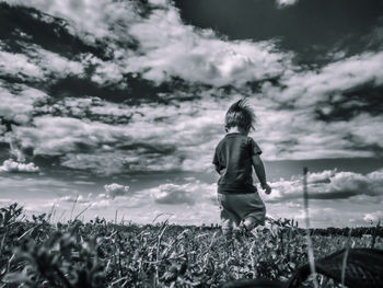 Rear view of boy walking on field against cloudy sky