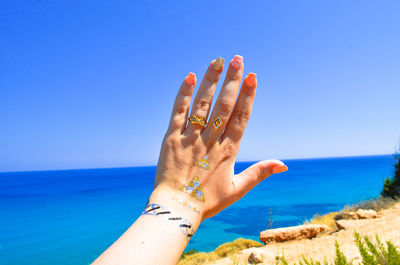 Cropped hand with temporary tattoo in front of sea