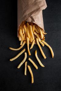 Hot crispy fries in a paper bag on a black background. tasty american fast food.