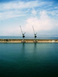 Cranes in sea against sky