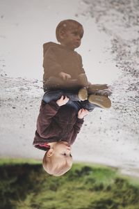 Upside down image of boy sitting by puddle on road