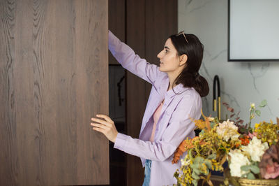 A cute girl is standing in the kitchen with an open cupboard and takes out groceries.