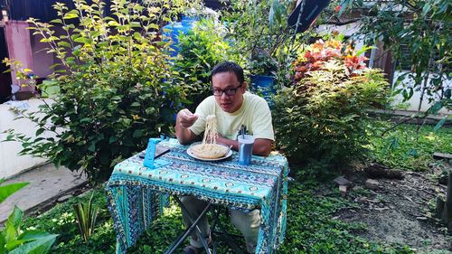 A grown-up man sitting and having breakfast on a table at yard. 