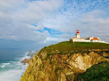 Lighthouse amidst sea and buildings against sky