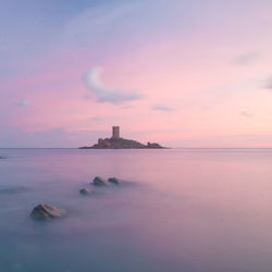 Scenic view of sea and island with castle against orange sky