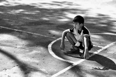 High angle view of boy crouching on road during sunny day