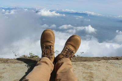 Low section of man sitting on mountain against sky