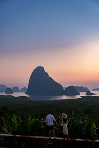 Rear view of people looking at mountain against sky during sunset