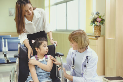 While the doctor comes to see her, a young asian girl patient smiles in her wheelchair.