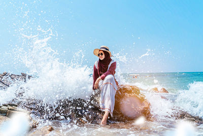 Woman sitting on rock by splashing sea