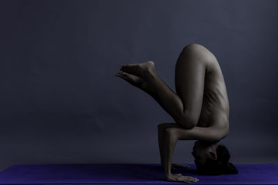 Full length of naked woman exercising against gray background