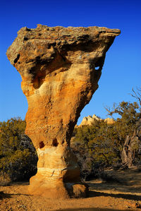 Tall red rock structure with trees against clear sky