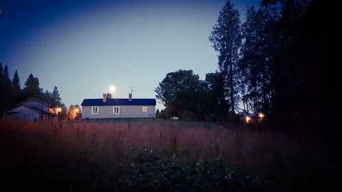 Illuminated road amidst trees against clear sky at night